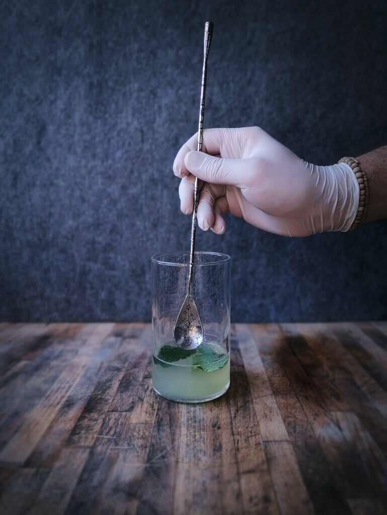 Fase due del procedimento. Aggiunta del ron e delle foglie di menta massaggiandole col cucchiaino.